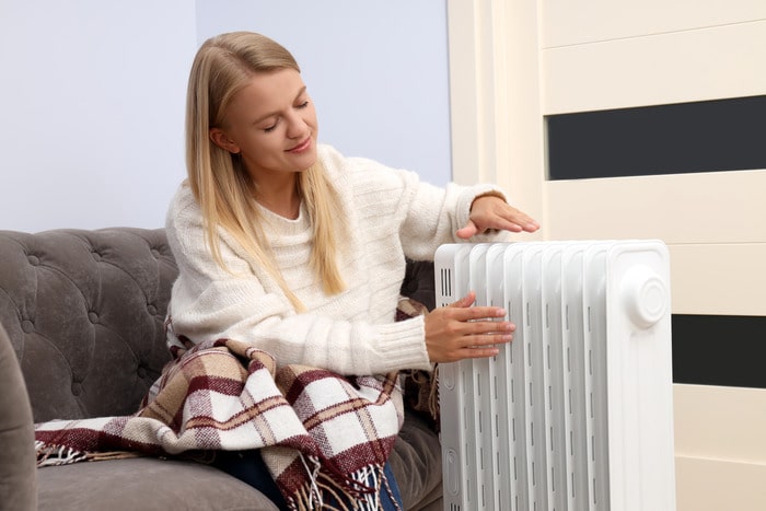 Woman sits on sofa by a boiler enjoying the warmth