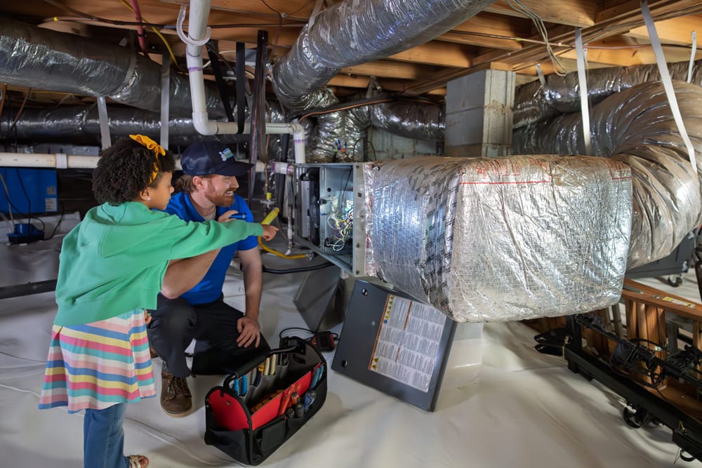 A Preferred Home Services technician uses a flashlight to inspect an air handler and filtration system in a clean, encapsulated crawl space to verify residential indoor air quality.