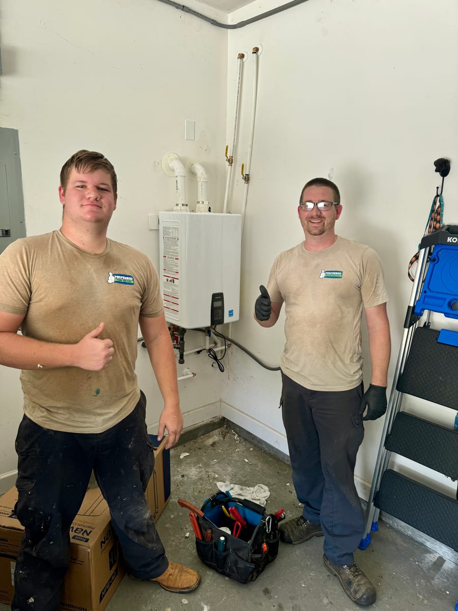 Two Preferred Home Services technicians give thumbs up after completing a tankless water heater installation in a residential garage.