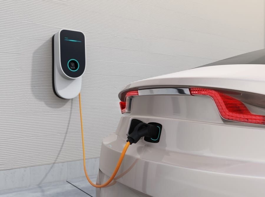 A white electric vehicle parked in a residential garage while connected to a professionally installed EV charger.