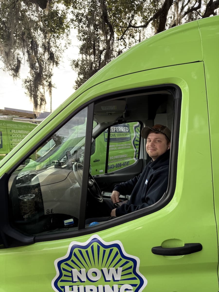 Smiling man sits in the cab of a bright green delivery van with a 'NOW HIRING' sign on the door behind him.