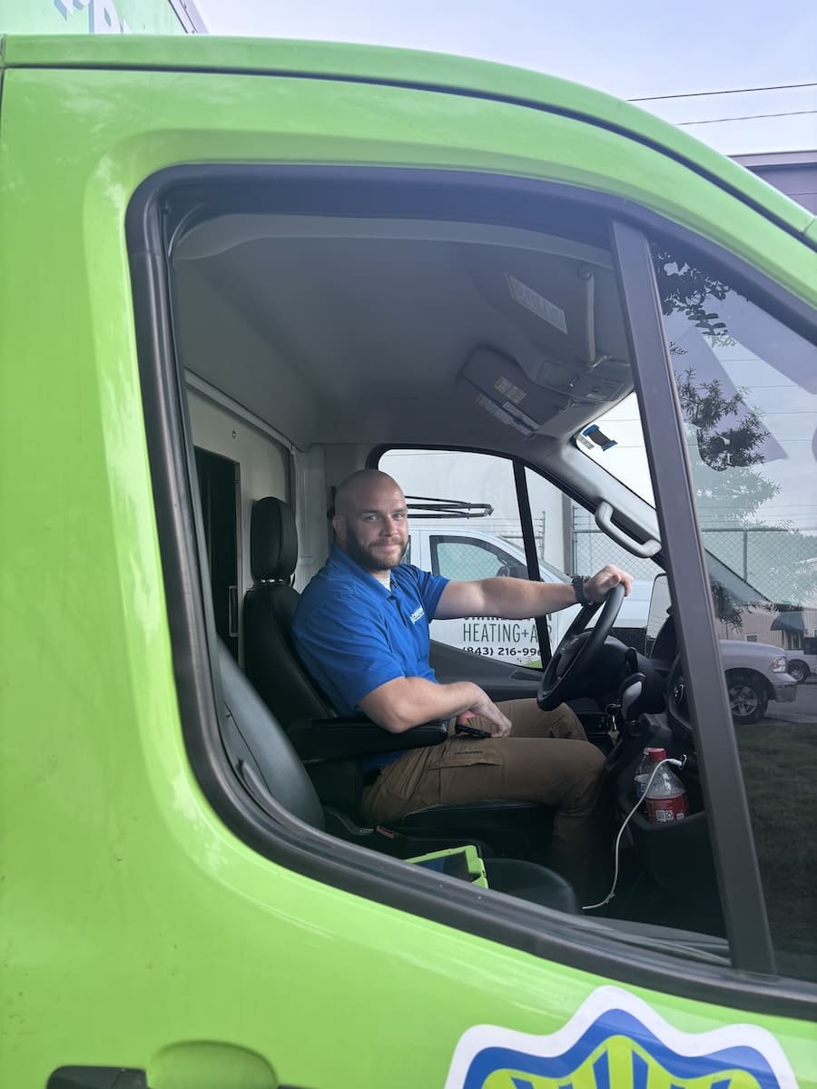 Man in a blue polo sits in the driver's seat of a bright green van, hands on the steering wheel and looking at the camera.