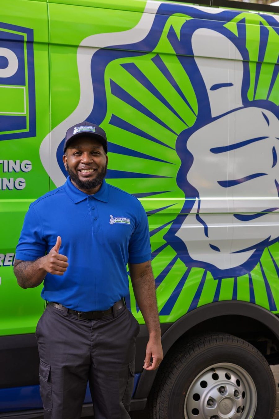 Smiling man in blue polo and cap giving a thumbs-up in front of a bright green vehicle with a large white and blue logo artwork.
