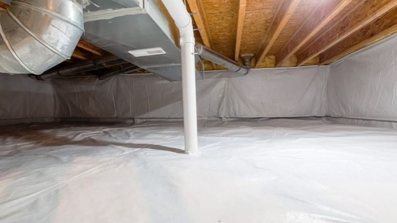Unfinished crawl space with white plastic on the floor, exposed wooden joists above, and a white vertical pipe in the center near HVAC ductwork.