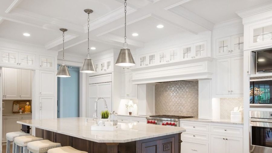Bright white kitchen with a large marble island, pendant lights, and stainless steel appliances.
