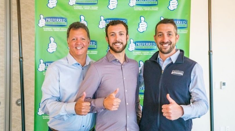 Three men in collared shirts pose and thumbs-up in front of a green backdrop branded with 'Preferred Home Services'.​​​​​]