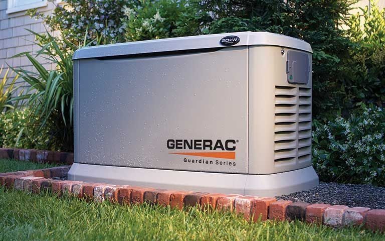 Outdoor Generac Guardian Series standby generator on a concrete pad with brick edging and greenery nearby.